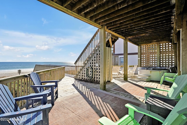 view of patio with a view of the beach, a hot tub, and a deck with water view