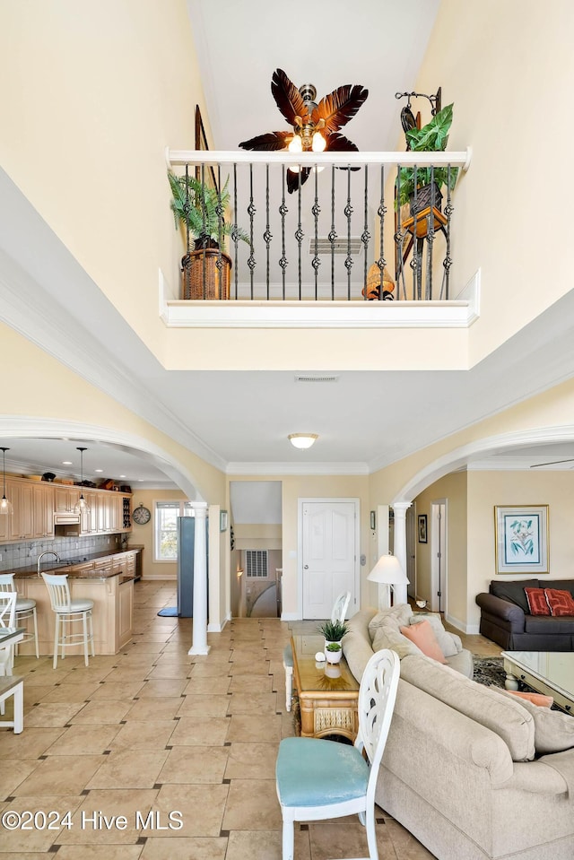 tiled living room with ornamental molding, decorative columns, ceiling fan, and a high ceiling