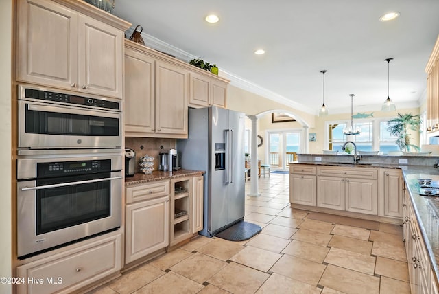 kitchen with pendant lighting, sink, appliances with stainless steel finishes, dark stone countertops, and ornate columns