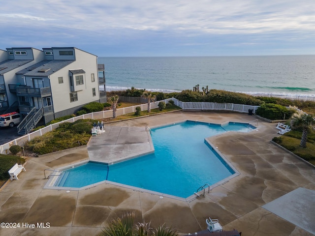 view of pool featuring a patio, a water view, and a beach view