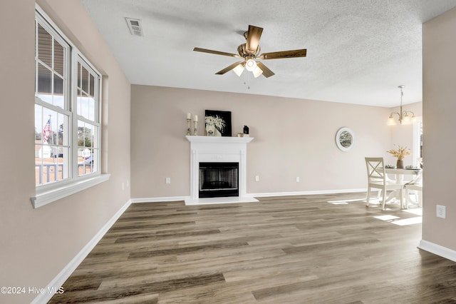 unfurnished living room featuring a textured ceiling, wood-type flooring, and ceiling fan with notable chandelier