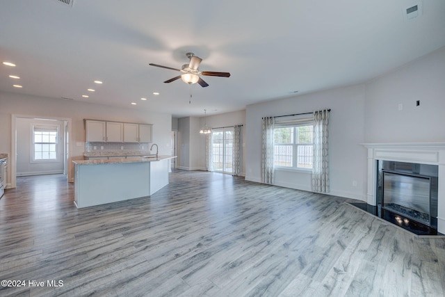 unfurnished living room featuring ceiling fan with notable chandelier, light wood-type flooring, and sink