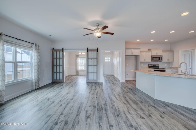 kitchen with light stone countertops, appliances with stainless steel finishes, a barn door, light hardwood / wood-style flooring, and white cabinetry