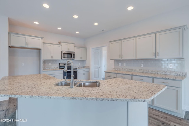 kitchen with sink, stainless steel appliances, light hardwood / wood-style flooring, an island with sink, and decorative backsplash