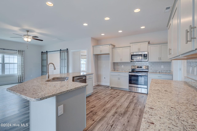 kitchen featuring a center island with sink, white cabinets, sink, light wood-type flooring, and appliances with stainless steel finishes