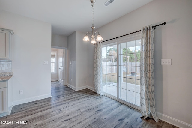 unfurnished dining area with light wood-type flooring, an inviting chandelier, and a wealth of natural light