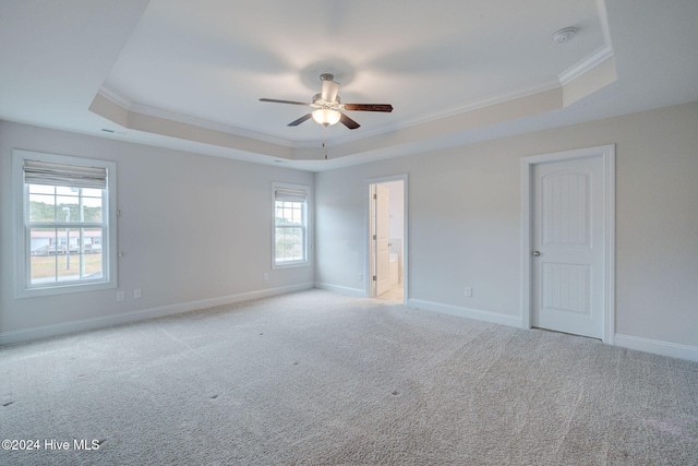 empty room with a tray ceiling, ceiling fan, crown molding, and light carpet