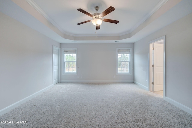 carpeted spare room with a raised ceiling, crown molding, plenty of natural light, and ceiling fan