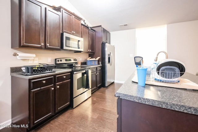 kitchen with appliances with stainless steel finishes, dark brown cabinets, and wood-type flooring