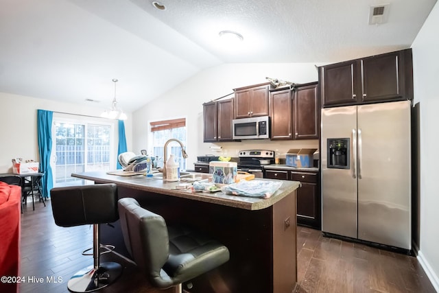 kitchen with dark hardwood / wood-style floors, stainless steel appliances, a kitchen island with sink, and vaulted ceiling