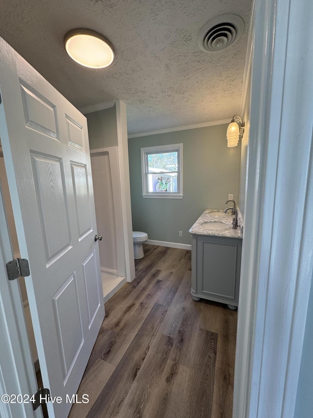 bathroom with wood-type flooring, a textured ceiling, toilet, vanity, and ornamental molding