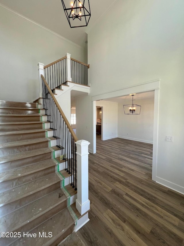 stairs with a high ceiling, crown molding, hardwood / wood-style floors, and an inviting chandelier