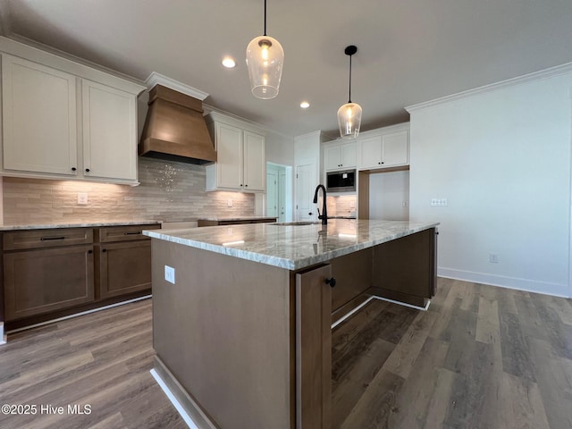 kitchen featuring pendant lighting, stainless steel microwave, white cabinetry, a large island, and wall chimney range hood