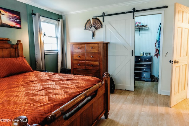 bedroom featuring a barn door, light hardwood / wood-style floors, and ornamental molding