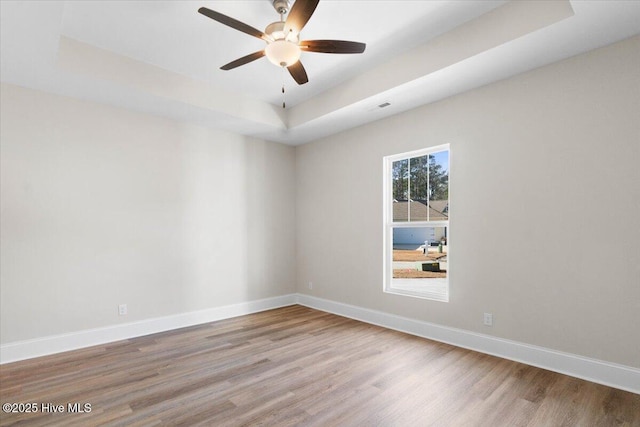 spare room featuring light hardwood / wood-style flooring, ceiling fan, and a tray ceiling