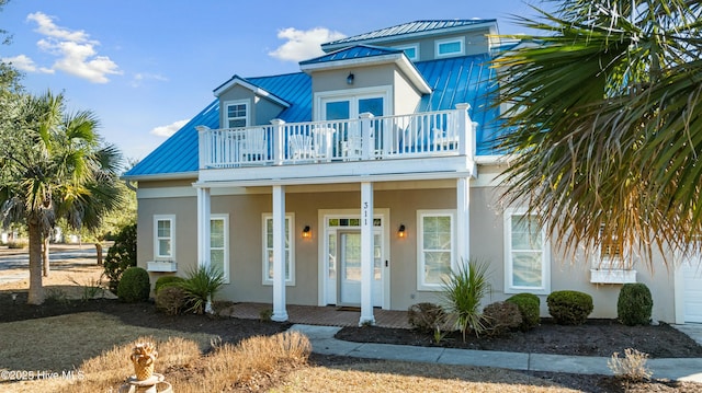 view of front of house featuring metal roof, a porch, a balcony, stucco siding, and a standing seam roof