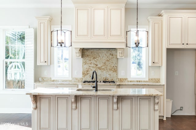 kitchen featuring light stone counters, a kitchen island with sink, crown molding, and decorative backsplash