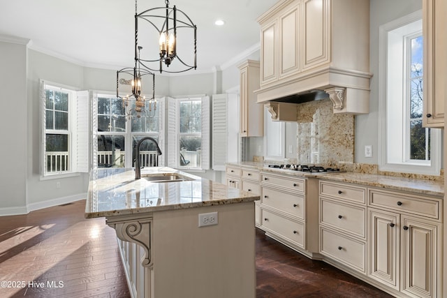 kitchen featuring crown molding, custom exhaust hood, cream cabinets, a sink, and a chandelier