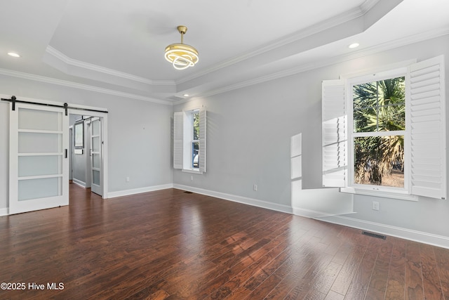 empty room with hardwood / wood-style floors, a barn door, visible vents, and baseboards