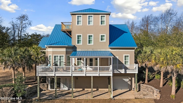 rear view of property with metal roof, an attached garage, a standing seam roof, a patio area, and stucco siding