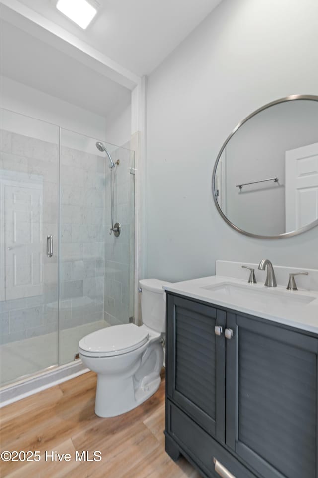 bathroom with toilet, a shower stall, wood finished floors, and vanity