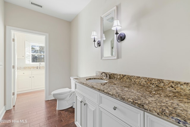 bathroom featuring toilet, wood finished floors, vanity, visible vents, and baseboards