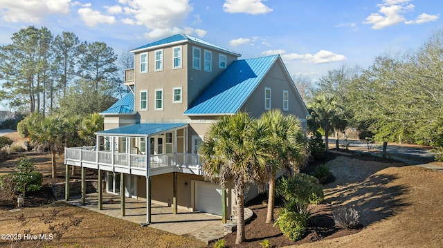 back of house with a garage, metal roof, a standing seam roof, and stucco siding