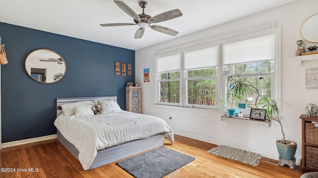 bedroom featuring ceiling fan, multiple windows, wood finished floors, and baseboards