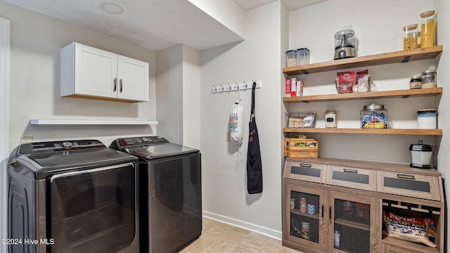 clothes washing area featuring washing machine and dryer, cabinet space, and baseboards