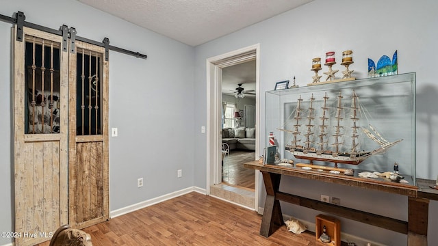 interior space with a barn door, baseboards, ceiling fan, wood finished floors, and a textured ceiling