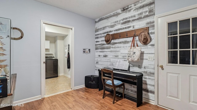 office area featuring a textured ceiling, wooden walls, light wood finished floors, and baseboards