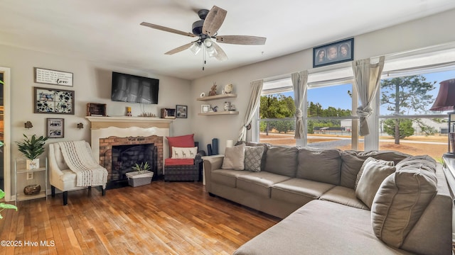 living room with a brick fireplace, wood finished floors, and a ceiling fan