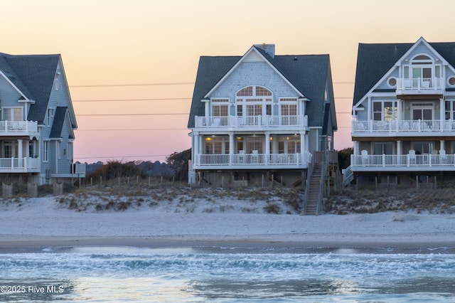 back of house at dusk featuring a water view and a view of the beach