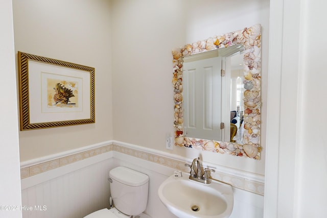 bathroom with toilet, a wainscoted wall, and a sink