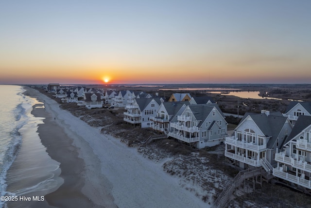 aerial view at dusk with a view of the beach, a water view, and a residential view