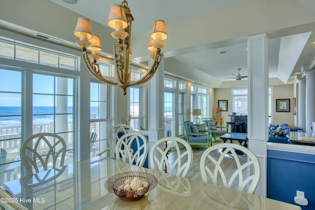 dining area featuring a water view, ornate columns, visible vents, and ceiling fan with notable chandelier