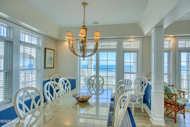 dining area with a healthy amount of sunlight, ornate columns, light wood-style floors, and an inviting chandelier