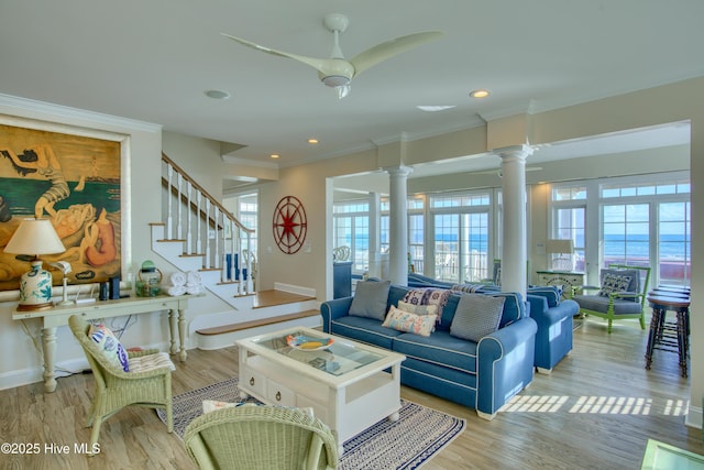 living area with crown molding, ornate columns, wood finished floors, baseboards, and stairs