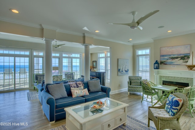 living room featuring a ceiling fan, a high end fireplace, light wood finished floors, and ornate columns