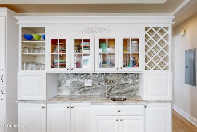 bar featuring light wood finished floors, electric panel, decorative backsplash, indoor wet bar, and a sink