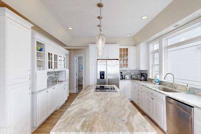 kitchen with a sink, white cabinets, appliances with stainless steel finishes, light wood finished floors, and glass insert cabinets