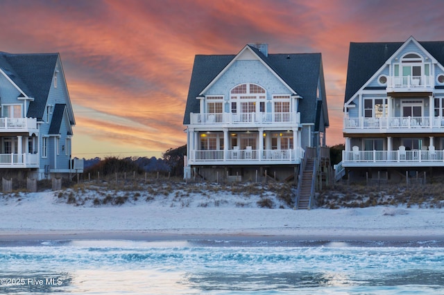 back of property at dusk featuring a water view and a view of the beach