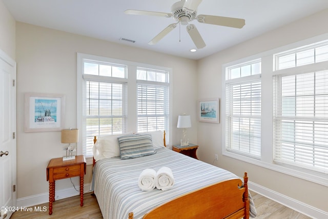 bedroom with a ceiling fan, visible vents, baseboards, and wood finished floors