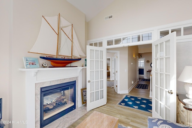 interior space featuring french doors, visible vents, a high end fireplace, wood finished floors, and high vaulted ceiling