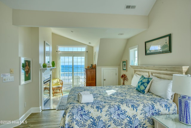 bedroom with lofted ceiling, multiple windows, wood finished floors, and a glass covered fireplace