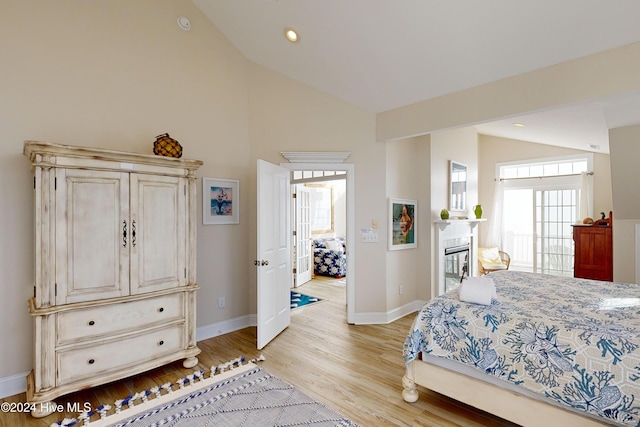 bedroom with vaulted ceiling, a glass covered fireplace, light wood-style flooring, and baseboards