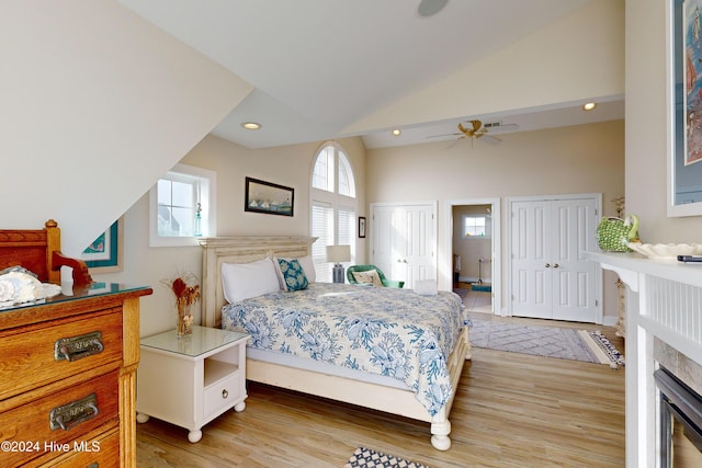 bedroom with light wood finished floors, vaulted ceiling, a fireplace, multiple closets, and recessed lighting