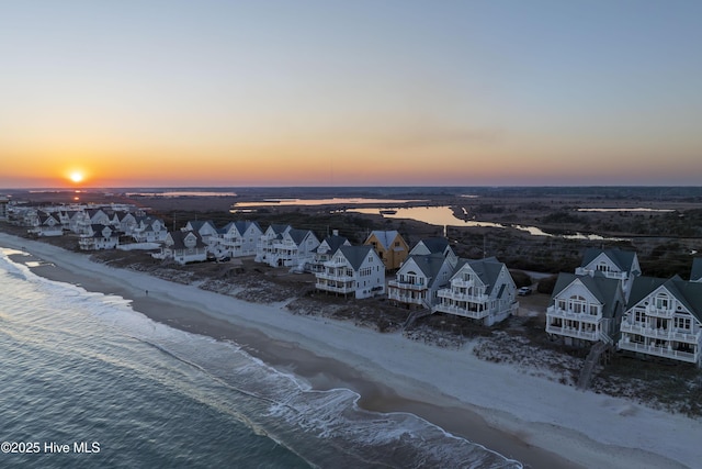 aerial view at dusk featuring a view of the beach, a water view, and a residential view