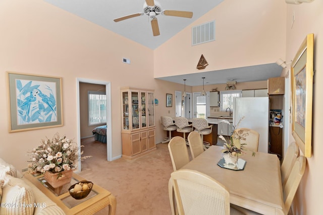 carpeted dining space with ceiling fan, sink, and high vaulted ceiling