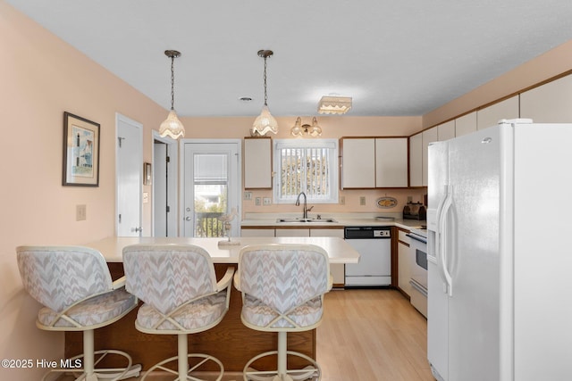 kitchen featuring white cabinetry, sink, white appliances, a breakfast bar area, and light wood-type flooring